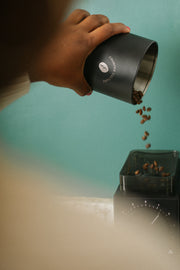 Photo of a person pouring coffee beans into a coffee grinder.